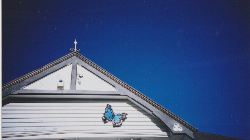 A fake blue butterfly sits on the white roof of a weatherboard home. 