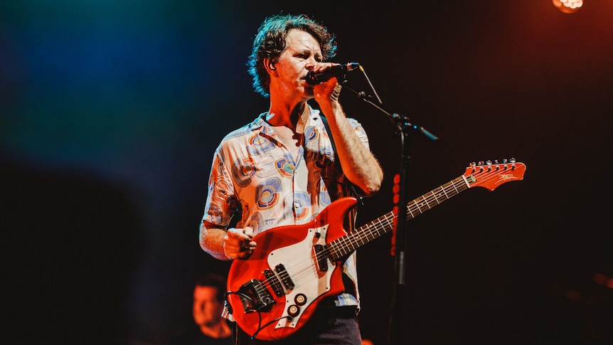 Bernard Fanning on stage with a red guitar singing into a microphone