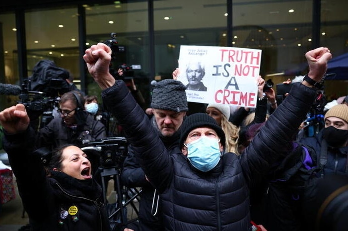 A masked man looks to the camera as he holds both his hands in the air in fists in celebration, in front of other celebrators.