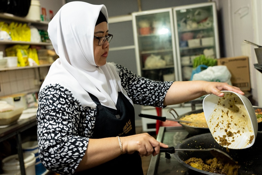A woman with a headscarf cooks over a gas stove