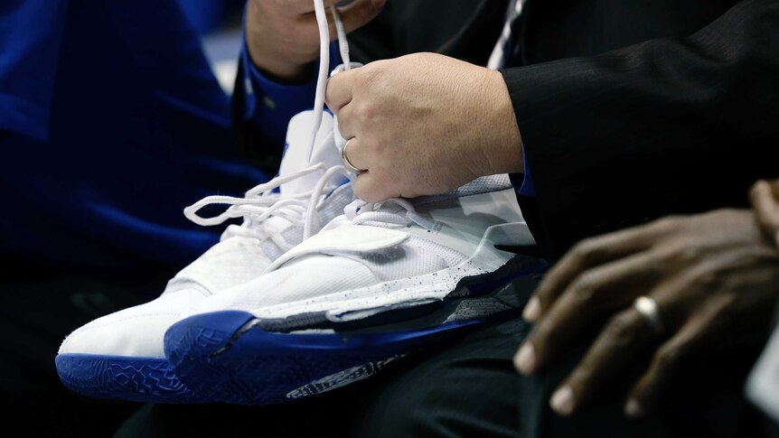 A man holds a pair of white nike trainers with blue soles