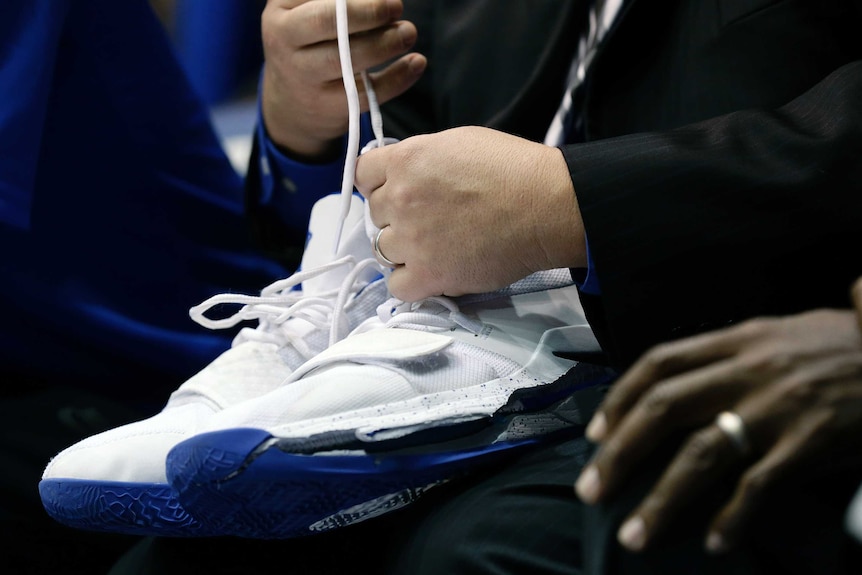 A man holds a pair of white nike trainers with blue soles