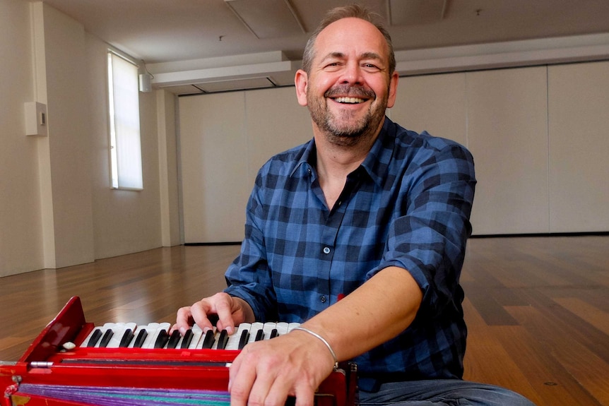 Kirtan musician Dave Stringer sitting in yoga studio with accordion.