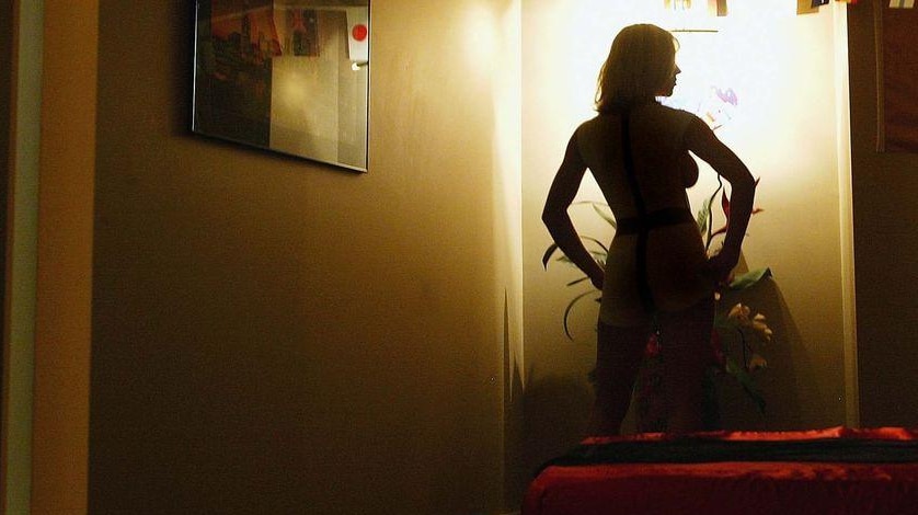 A prostitute stands in a room in a brothel.
