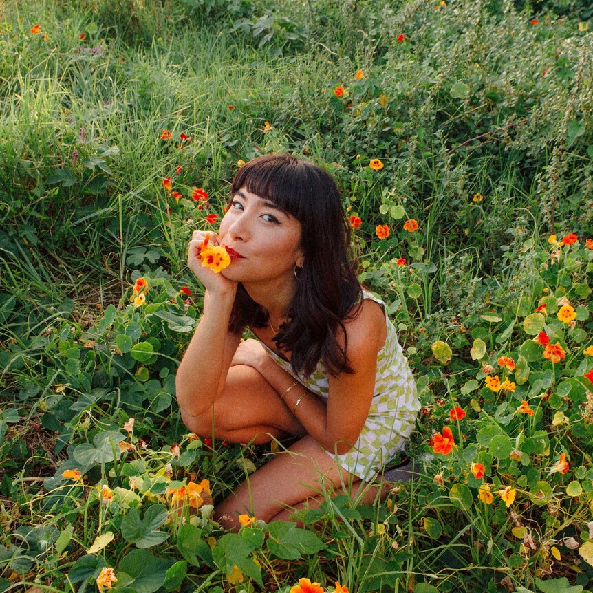 Linda Marigliano sitting down in a field of grass with flowers.