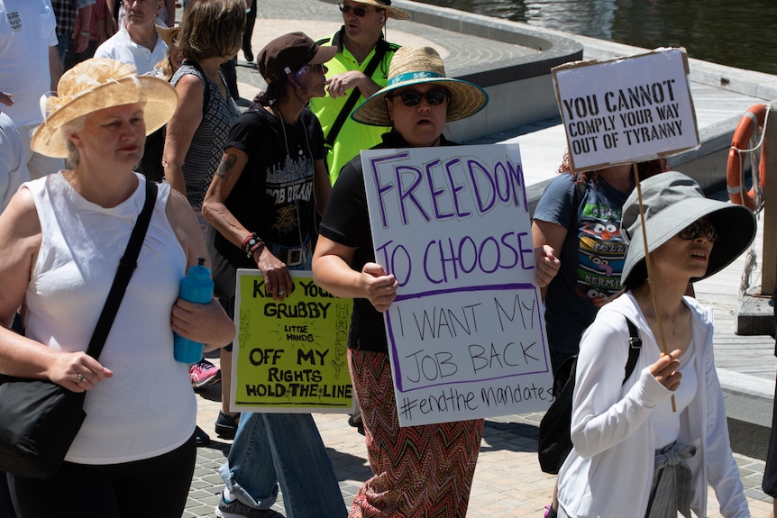 Protesters hold signs saying 'freedom to choose, I want my job back'