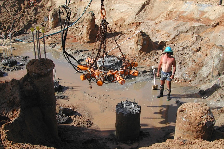 Piece of infrastructure being craned into large hole as construction workers supervises