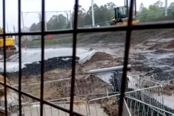 A creek next to a railway construction zone fills with silt and runoff — as viewed through a fence.