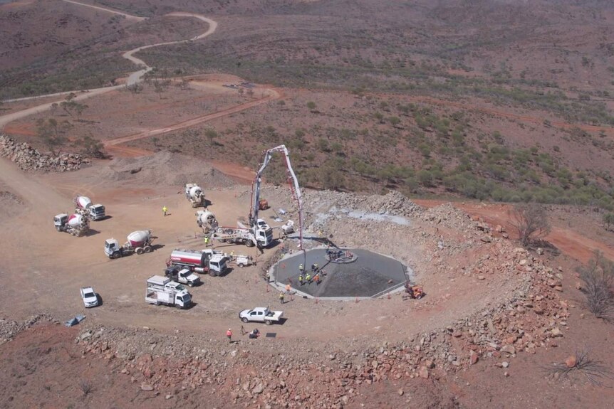 An aerial shot of trucks and cranes surrounding a concrete base which is in the process of being poured.