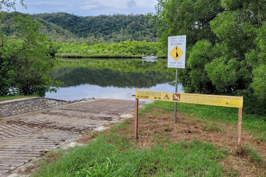 A crocodile warning sign at a boat ramp leading down to a river.