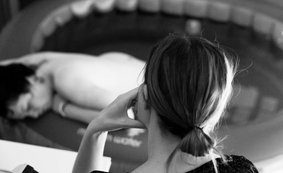 Woman labours in a pool with midwife watching over her