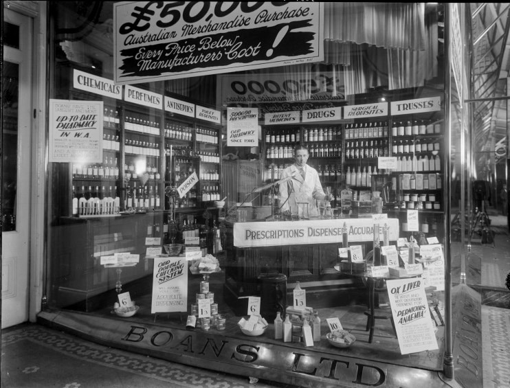 Fotografía en blanco y negro de una farmacia con mostrador y muchos estantes para botellas.