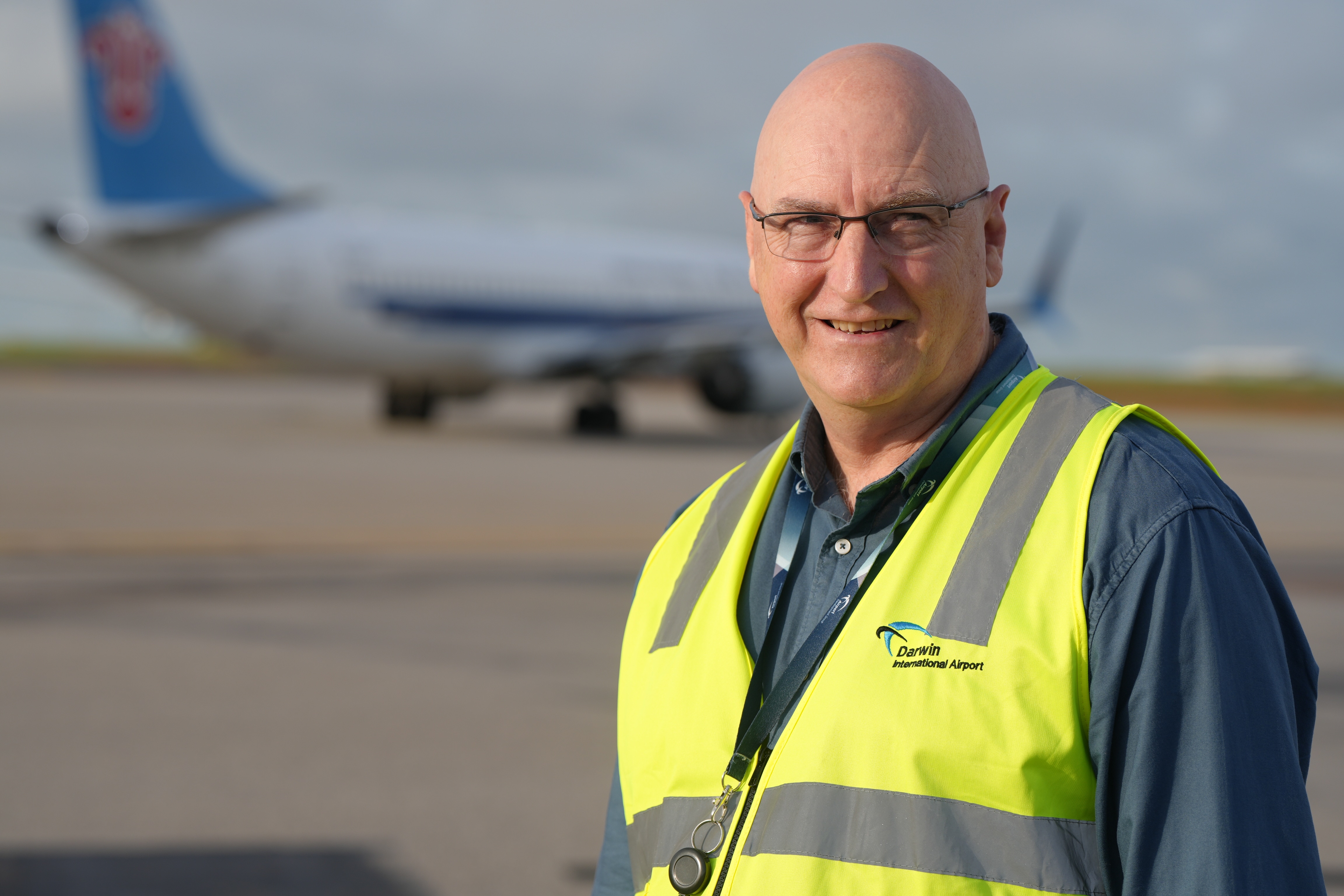 Ao fundo você pode ver um homem vestindo um colete de trabalho de alta visibilidade e um avião comercial.