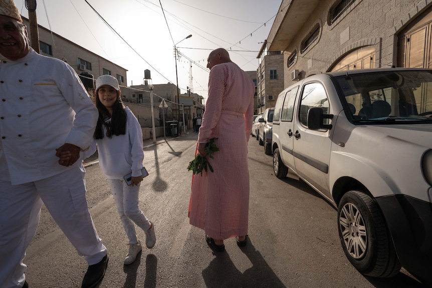 A small girl in white clothing grins while holding an older man's hand