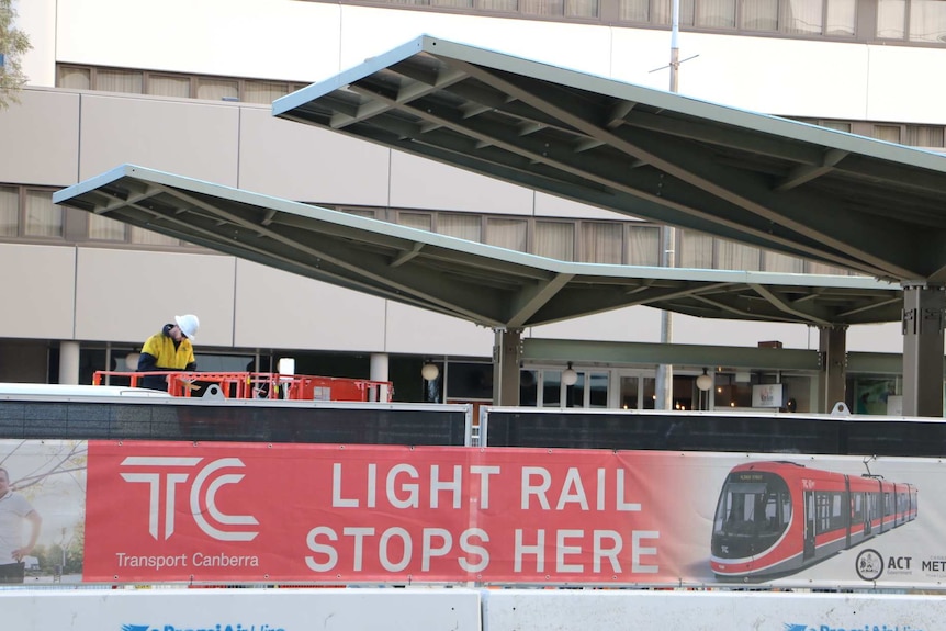 A sign reads "light rail stops here" in front of workers erecting light rail stops on Northbourne Avenue.