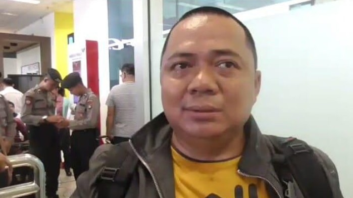 A man talking to a camera with crowd at the airport at the background