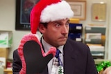 Steve Carrell's character Michael Scott wears a santa hat and looks furious at his gift of a pink hand-knitted oven mitt.