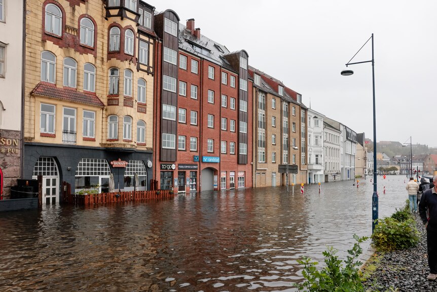 A flooded city street in northern Europe with people walking along higher path