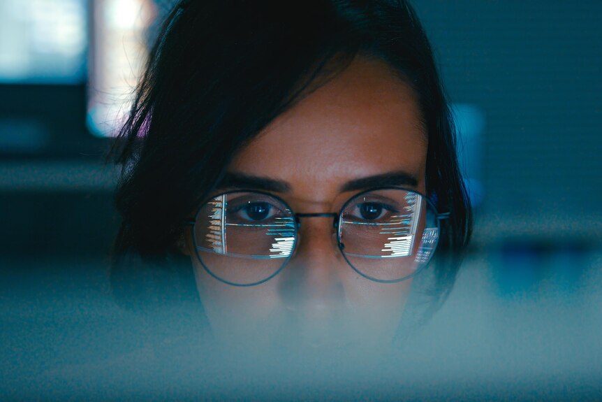 Close up of eyes of woman wearing glasses, with laptop screen reflecting in the glasses.