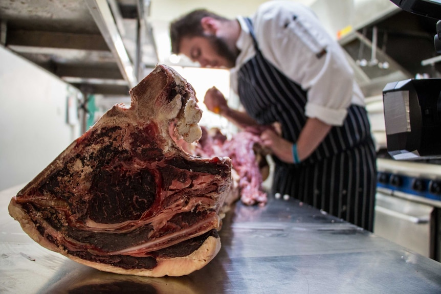 A regional Victorian chef cuts pieces of meat from a cow carcass.