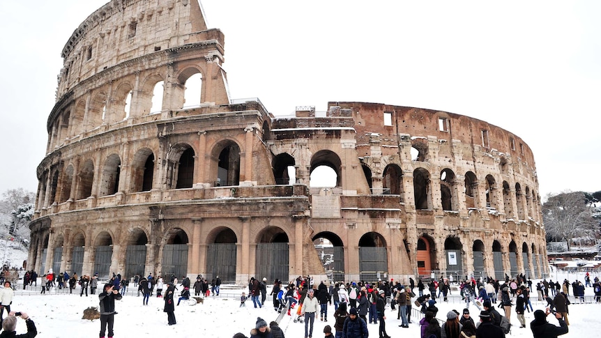 People stand in front of the Colosseum as snow blankets Rome