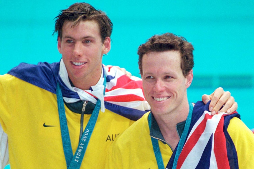 Two swimmers have medals around their necks and Australian flags around their shoulders.