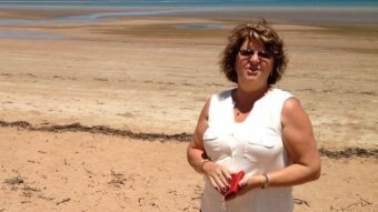 A woman standing on a beach holding her wallet.