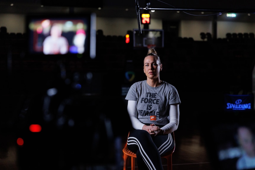 Tess Madgen sits on a stool, with a microphone overhead. She wears a shirt that says 'the force is female'