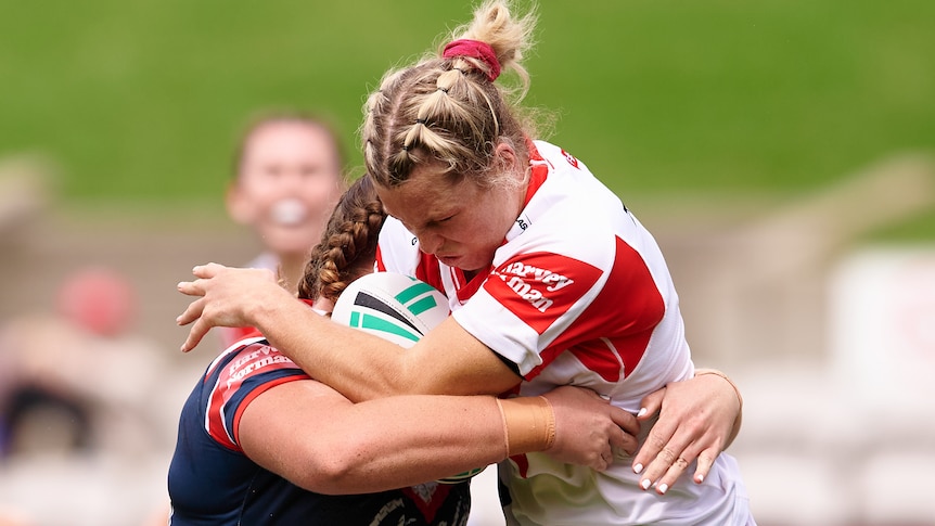 A St George Illawarra NRLW player holds the ball as she is tackled by a Sydney Roosters opponent.