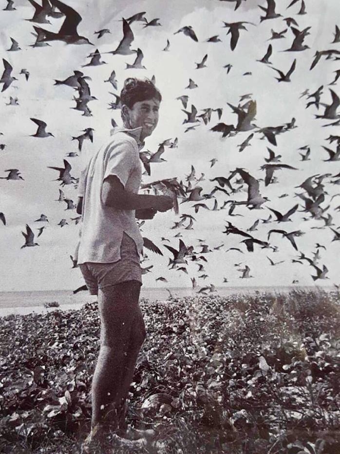King Charles as a young man on remote Upolu Cay, with a big grin and surrounded by hundreds of birds in the air.