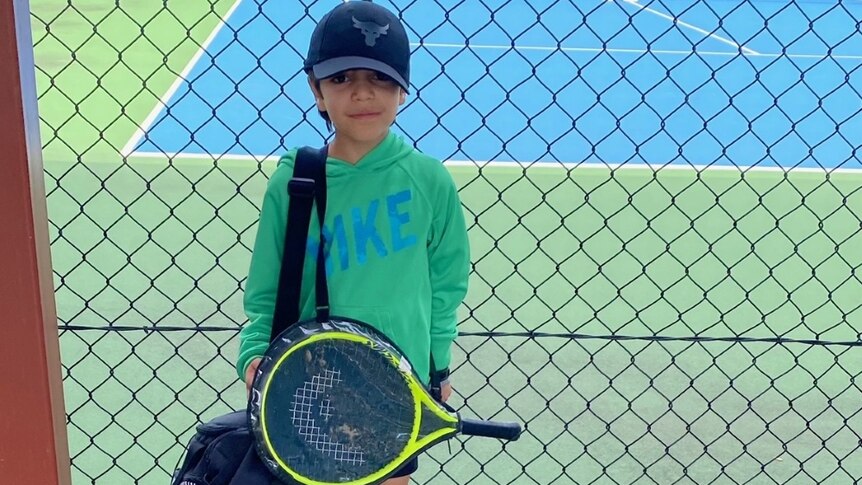 Samyar (6) stands on the tennis court holding a tennis racquet.