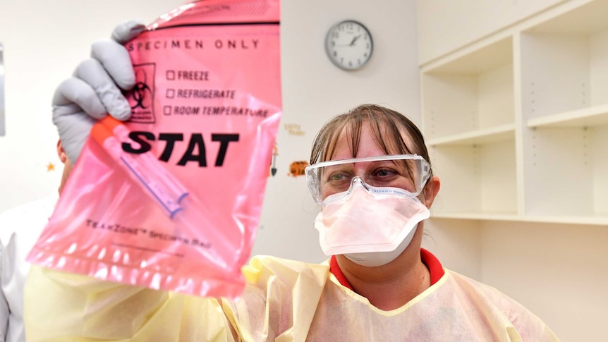 A nurse wearing a face mask holds up needles inside a bag in a fever clinic.