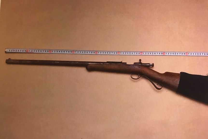 A Winchester rifle placed on a table with measuring tape above it