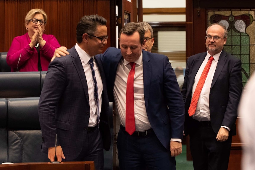 Ben Wyatt and Mark McGowan with their arms around each other in State Parliament as other MPs look on.