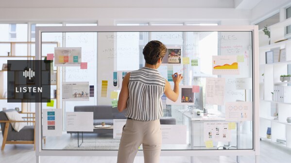 woman in modern office brainstorms on glass wall with marker and post it notes. Has Audio.
