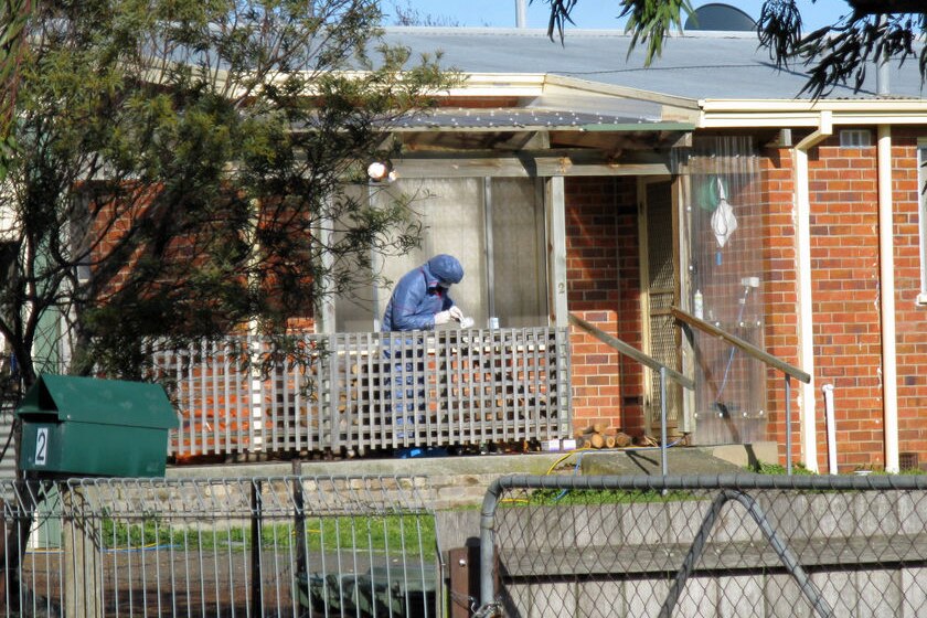 A forensics police officer working on the front porch of a suburban house.