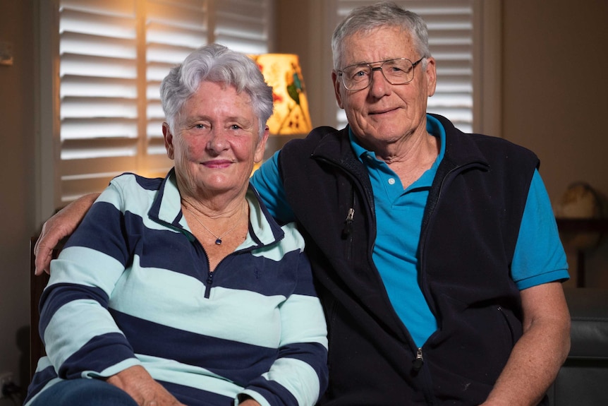 Cathy and Bill Kleinmuelman sitting next to each other on a sofa with Bill's arm around Cathy's shoulders