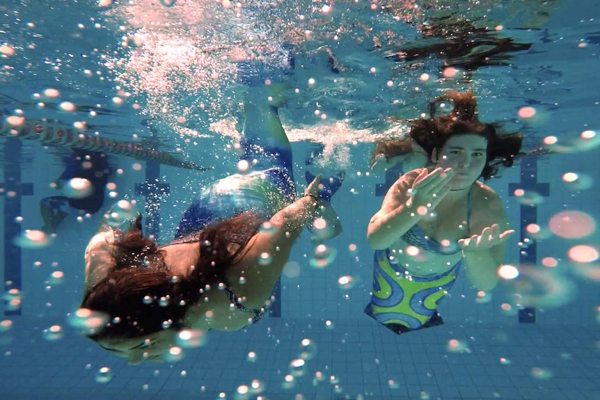 Young women dressed as mermaids swim underwater