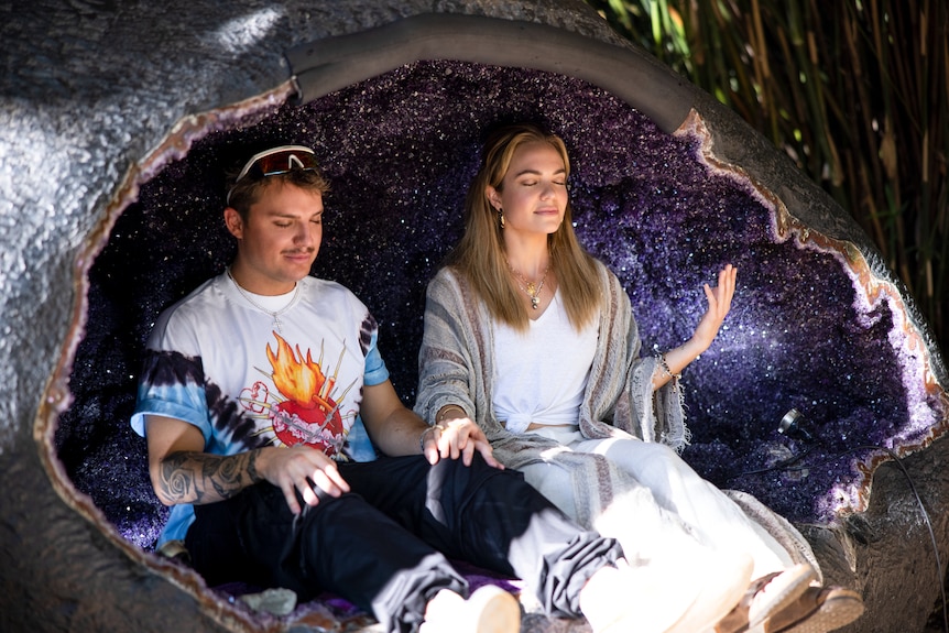 A young man and a young woman sit together with their eyes closed serenely