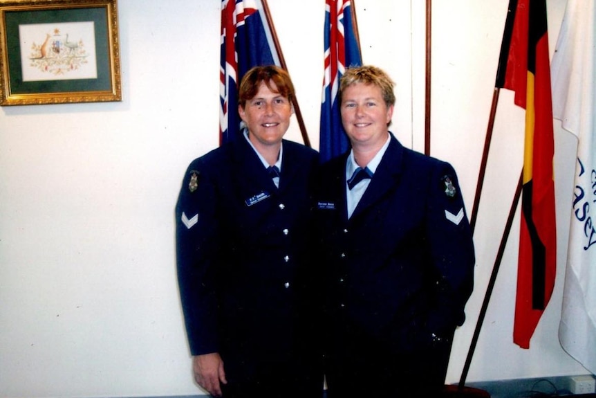 Two women in police uniforms stand in front of Australian flags in the early 2000s.