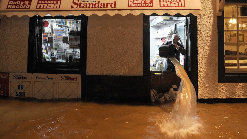 A shopkeeper used a bucket to bail floodwater out the front door of his shop at night.