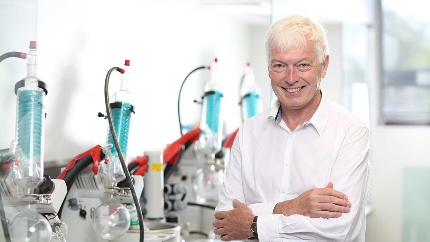 man with white hair and white shirt standing with arms crossed and smiling in a lab