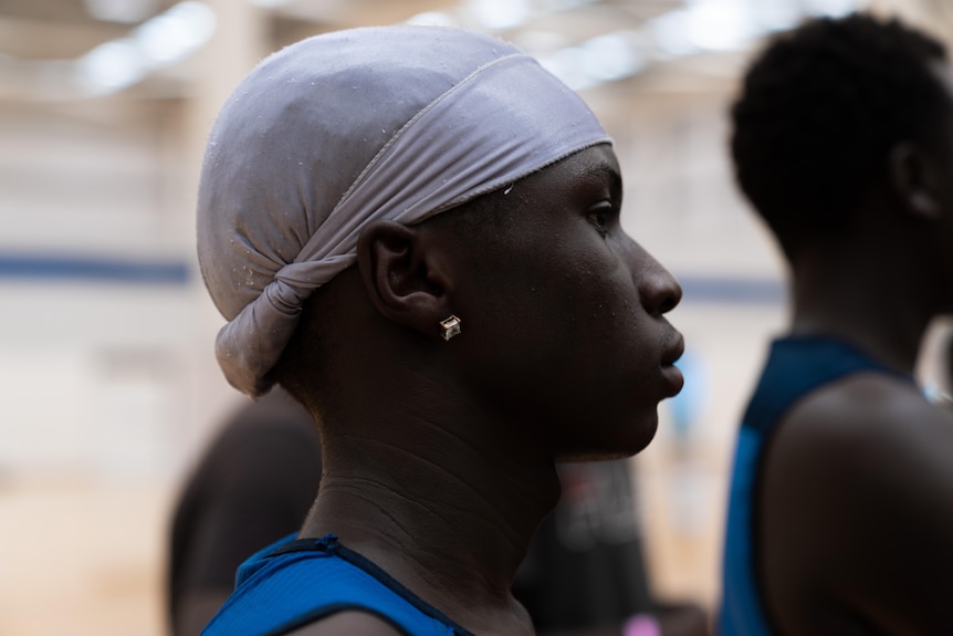 A close up shot of an African teenage boy looking onto a basketball court 
