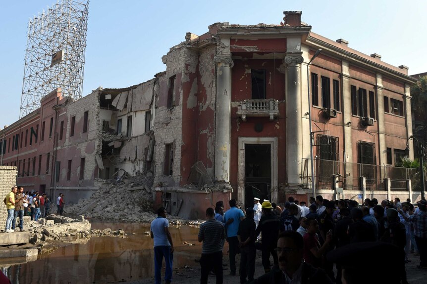 Egyptian security and citizens look at the the destroyed facade of the Italian consulate building