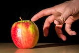 A person reaches for a red apple.