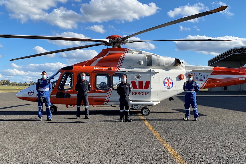 Four men, dressed in paramedic and pilot uniforms, stand in front of a helicopter