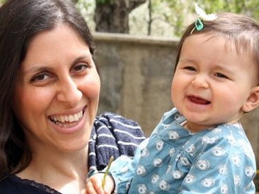 A smiling woman holds a baby and poses for a photograph.