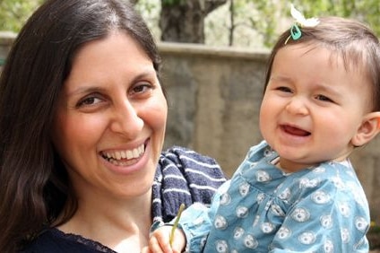 A smiling woman holds a baby and poses for a photograph.