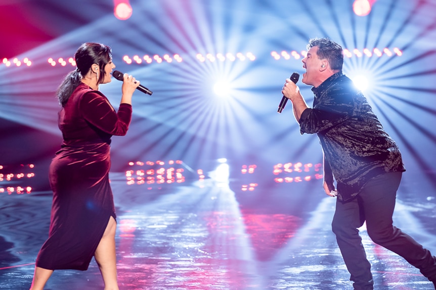 Amanda wearing a deep red gown singing on stage with James.