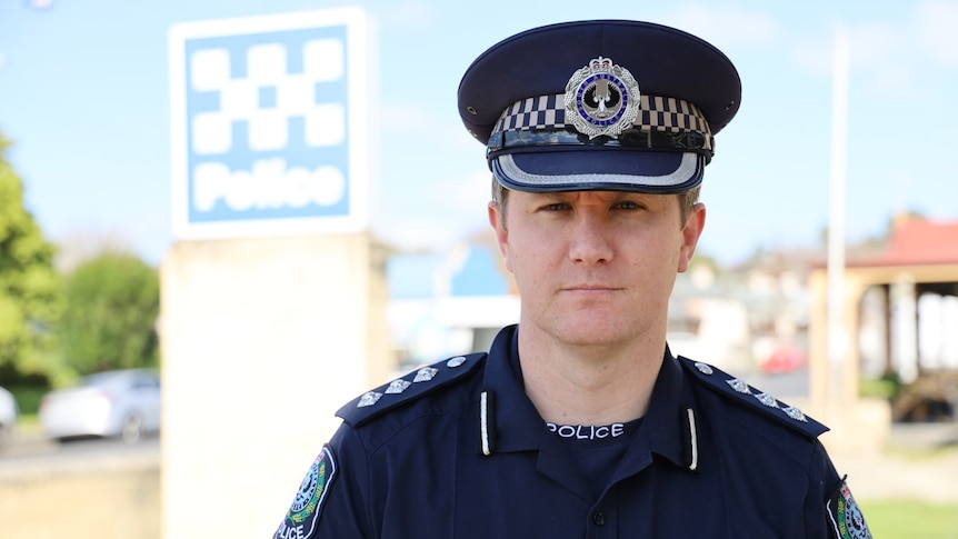 A policeman wearing a dark blue peaked hat in front of a police sign